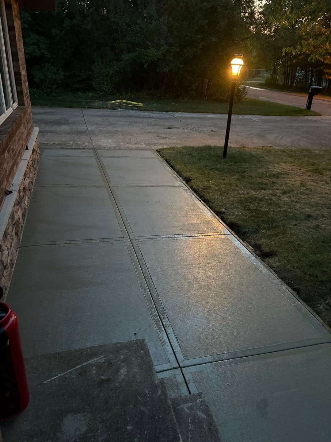 Freshly poured concrete walkway illuminated by a lamp in a scenic residential setting.