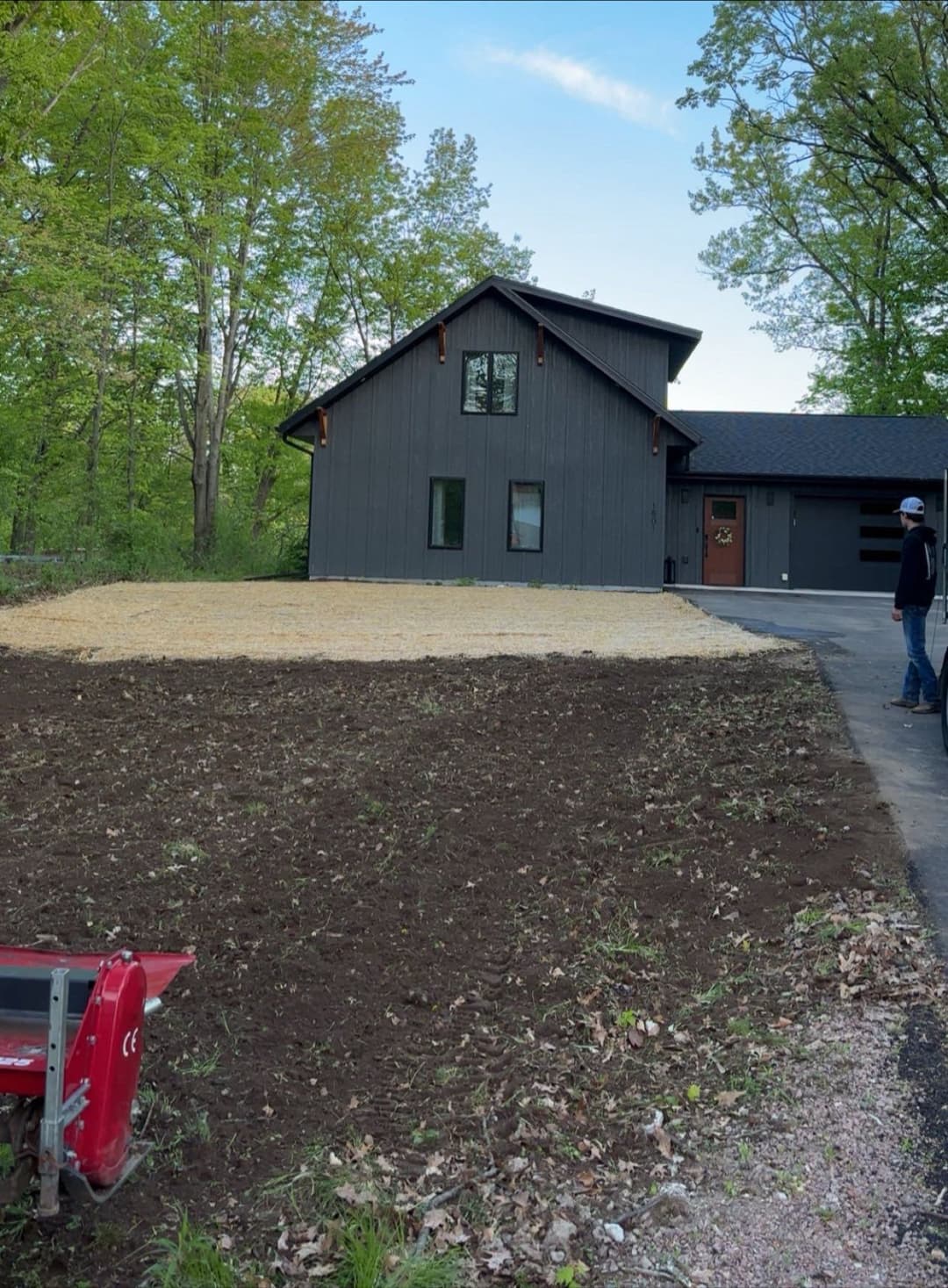 Modern house in wooded area with freshly tilled garden space and landscaping equipment nearby.