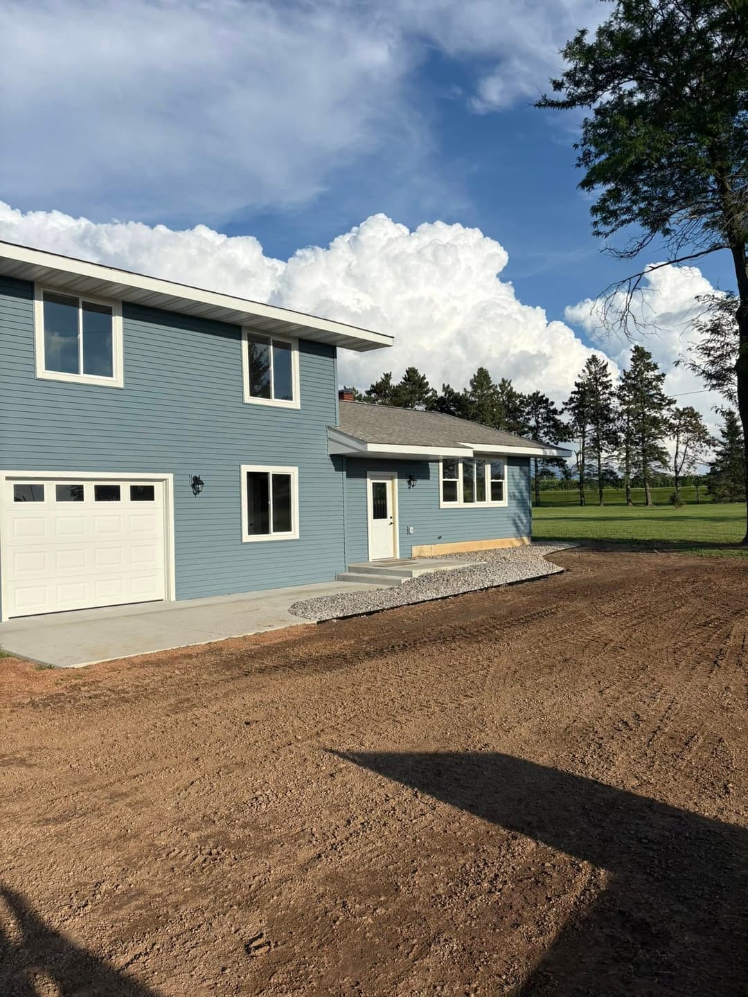 Modern blue house with garage, surrounded by open land and a clear sky with clouds.