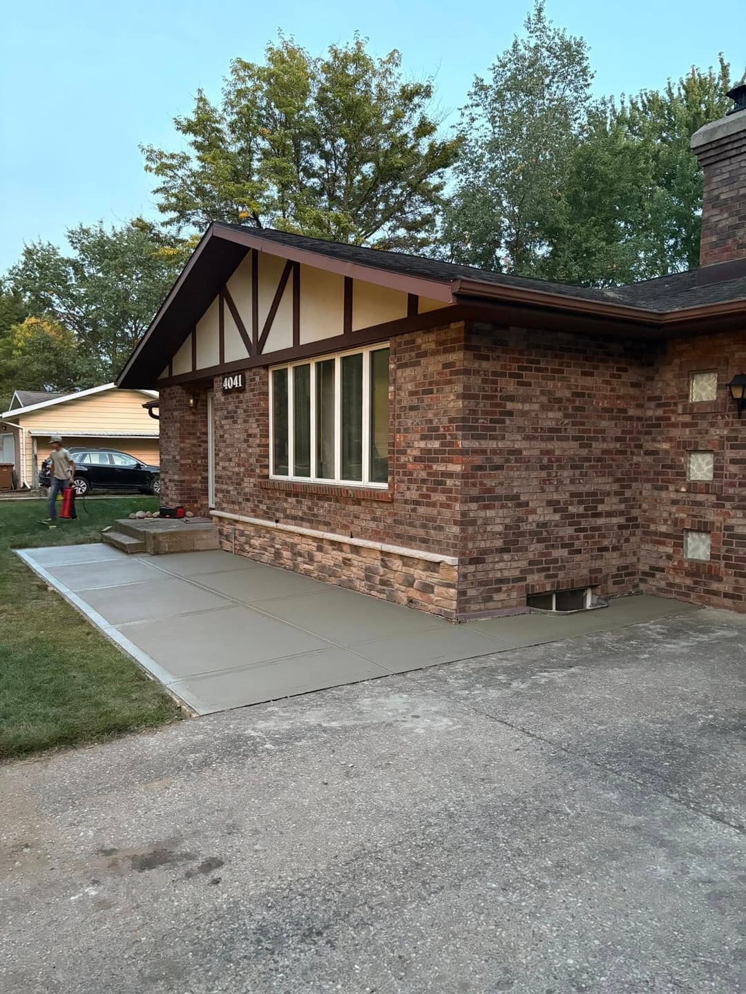 Brick house with large windows and newly poured concrete walkway in residential area.