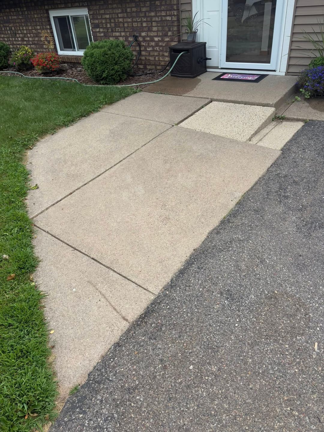 Sidewalk transition from concrete to asphalt with grass border and front door area.