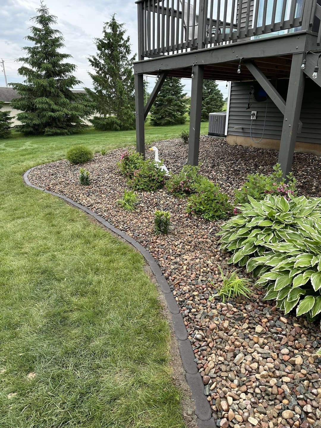 Landscaped garden with rocks, shrubs, and a white statue under a deck in a residential area.