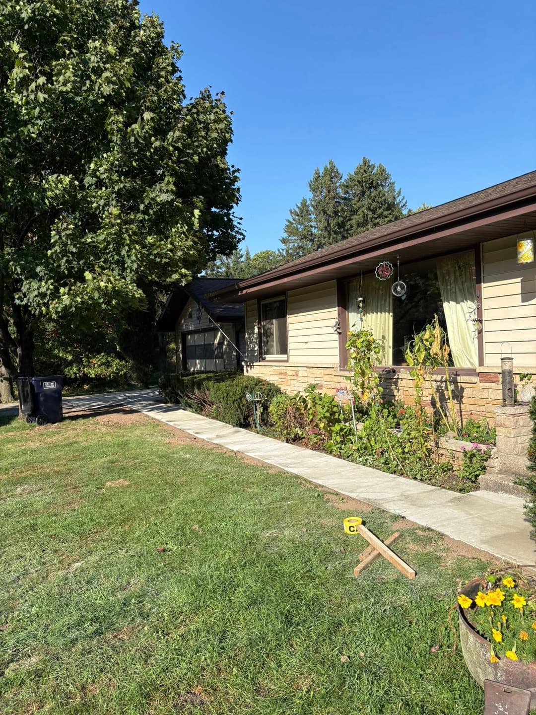 Single-story house with manicured lawn, tree shade, and garden path on a sunny day.