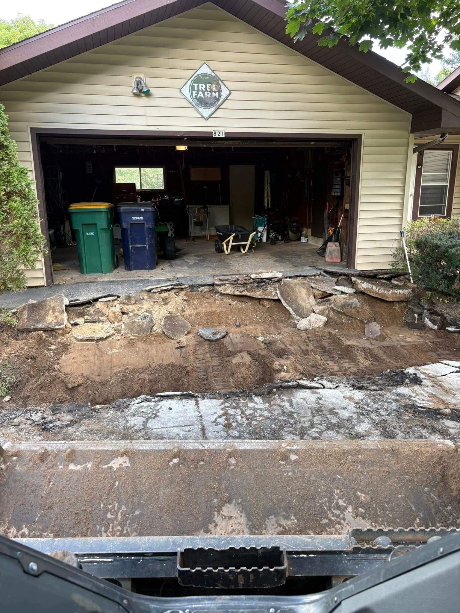 Excavation site in front of garage, showing exposed foundation and construction debris.