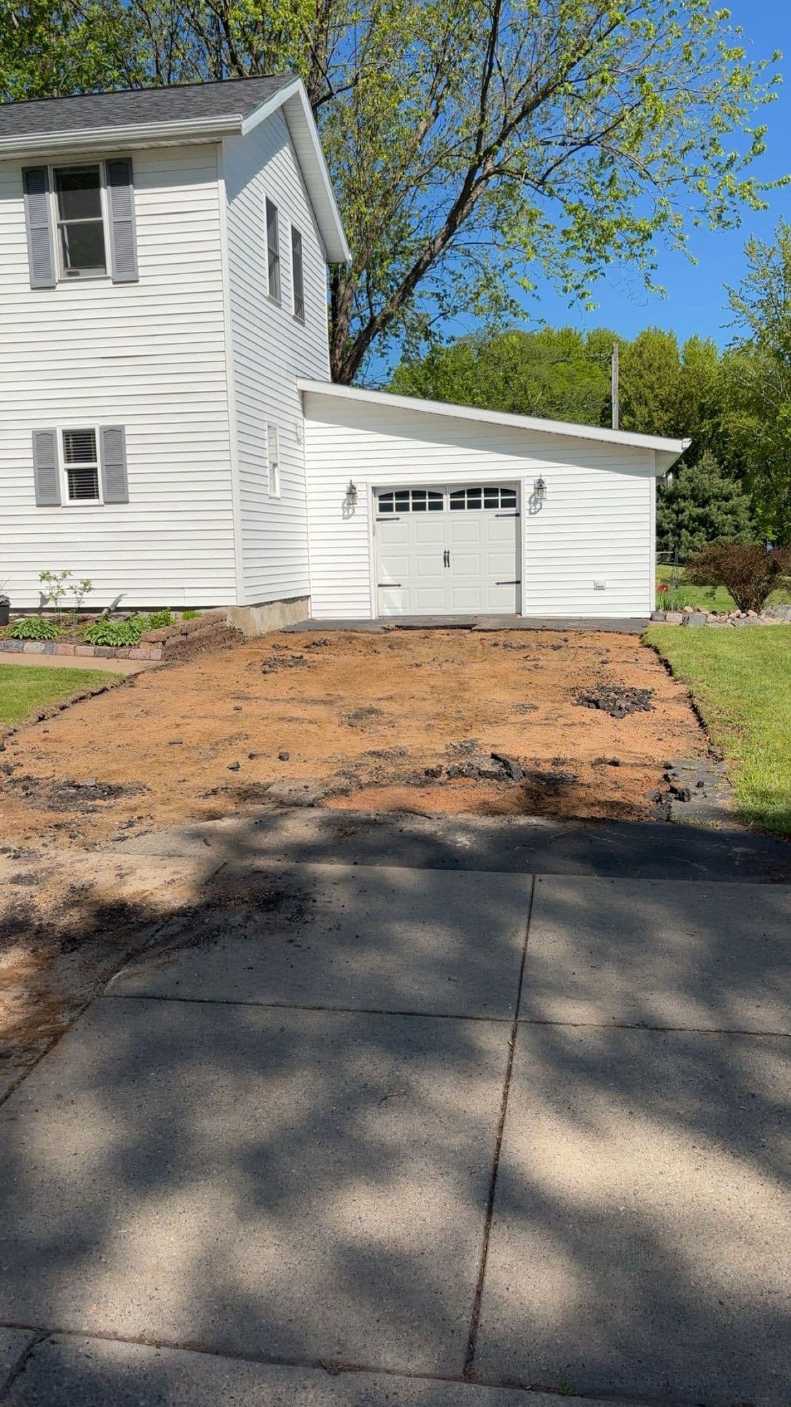 Freshly leveled driveway area in front of a white house with garage and green landscaping.